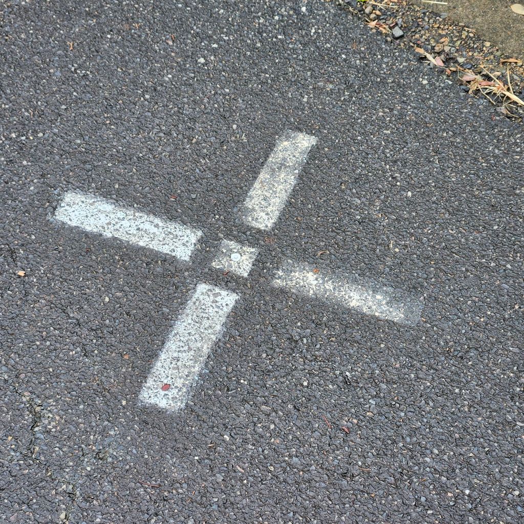 White painted ground control point marking on asphalt surface